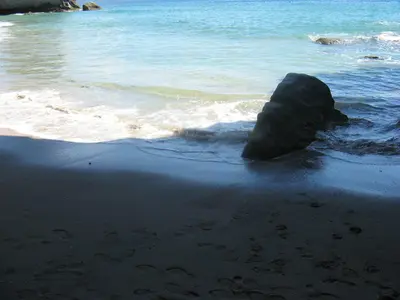Dunkler Sandstrand mit einem einzelnen Felsblock in der Brandung